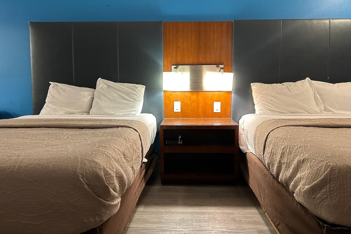 A hotel room with two beds, a wooden headboard, and a nightstand with a lamp.