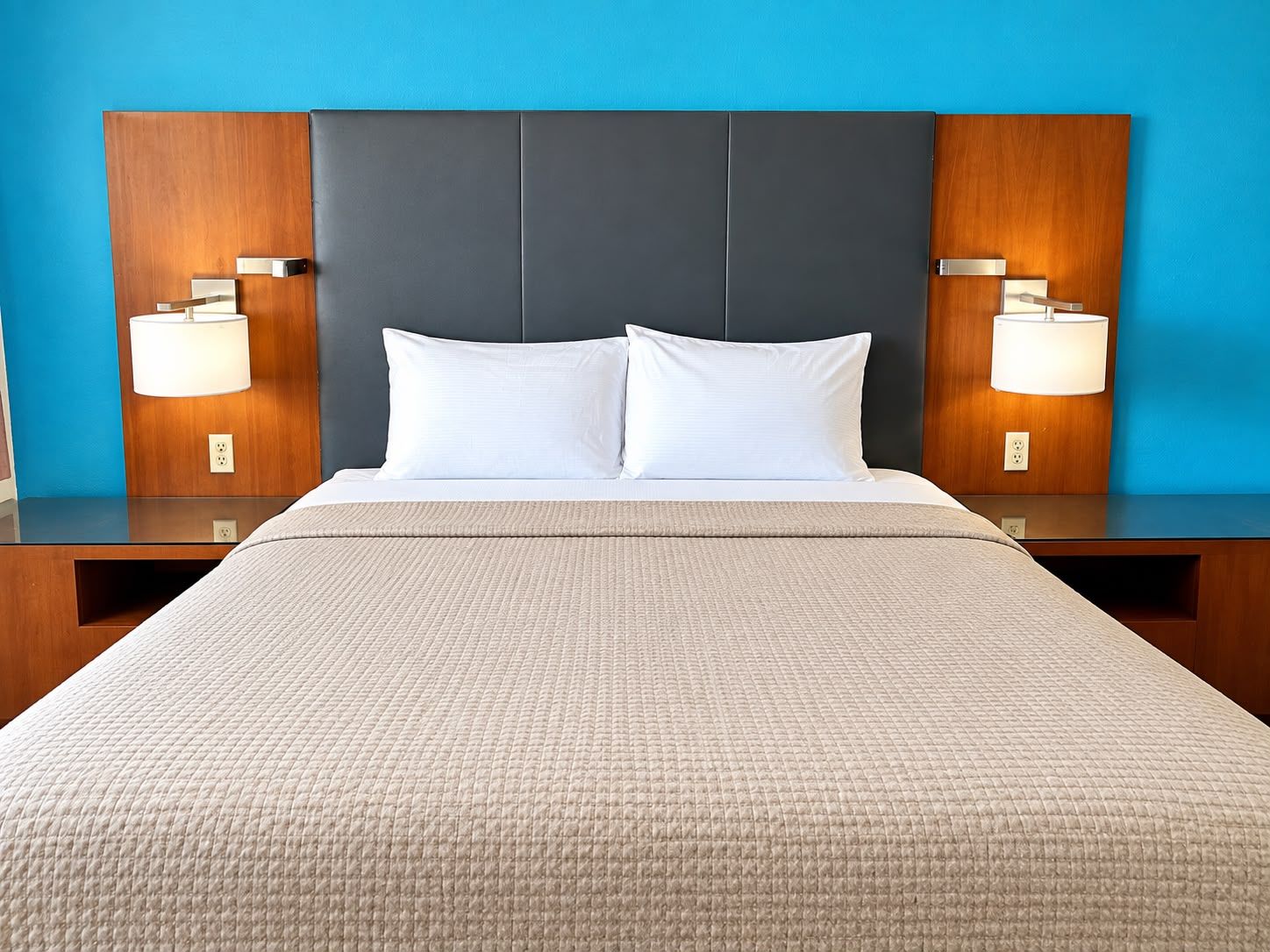 Una habitación de hotel con una cama grande, dos lámparas de noche y una pared azul.
