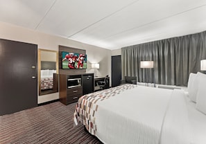 A hotel room with a bed, a desk, a television, a mirror, and a window with curtains. - Red Roof Inn Reading (Reading)
