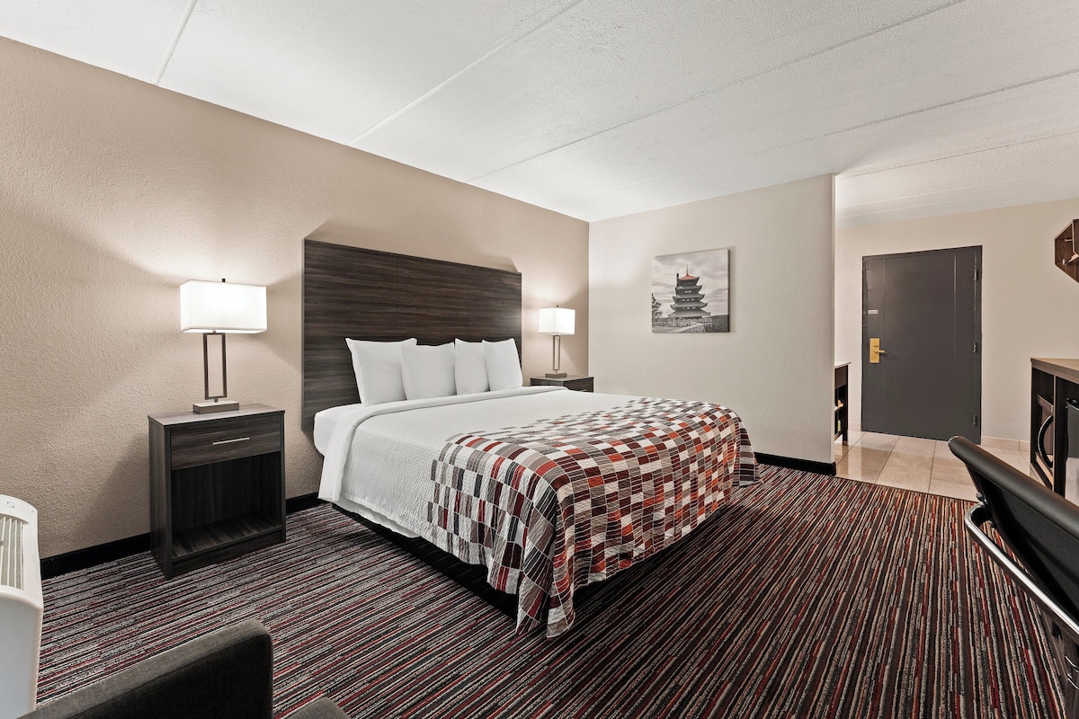A hotel room with a large bed, a nightstand, a desk, and a chair.