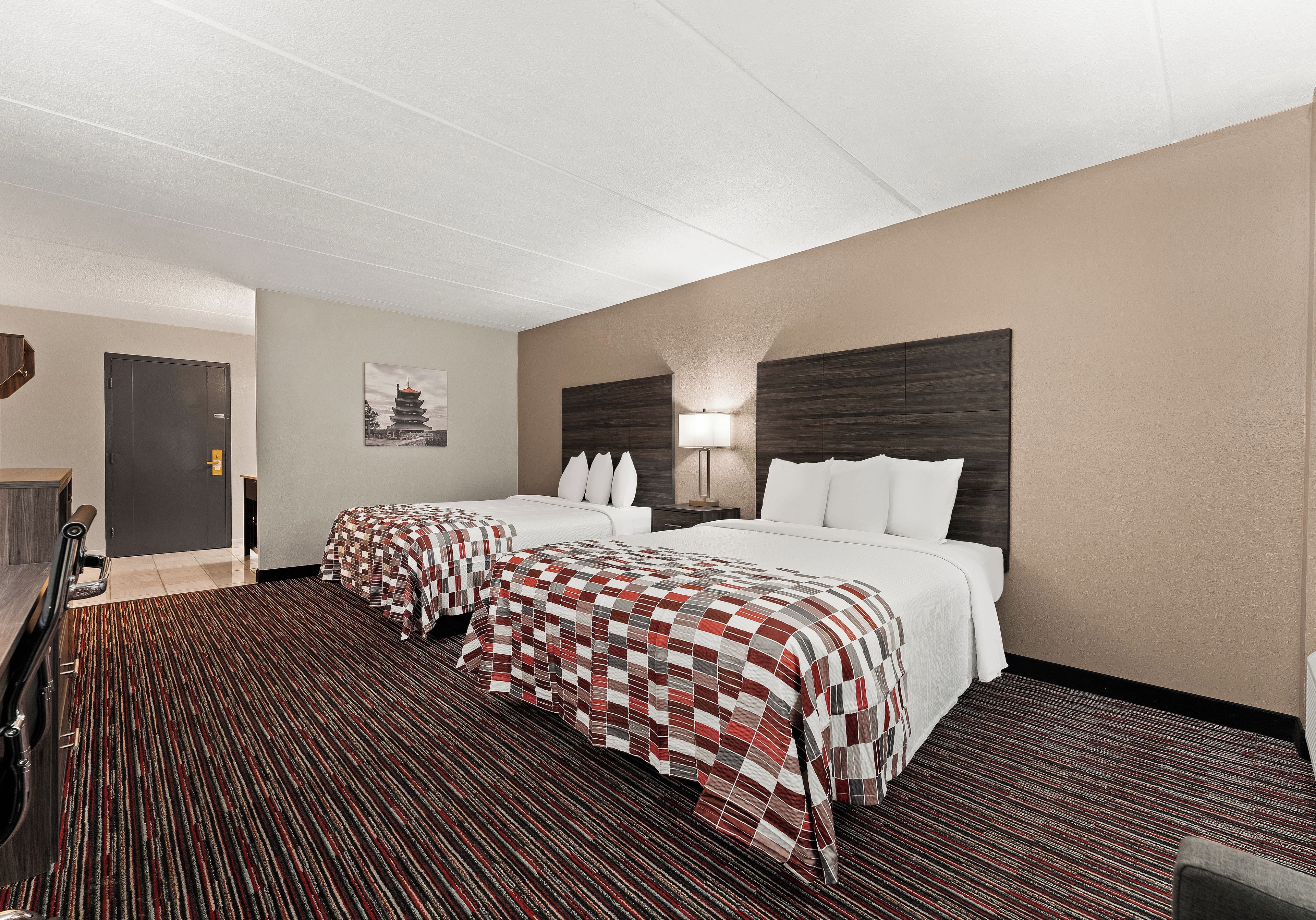 Habitación de hotel con dos camas, un escritorio, una silla, una lámpara y una obra de arte colgada en la pared.