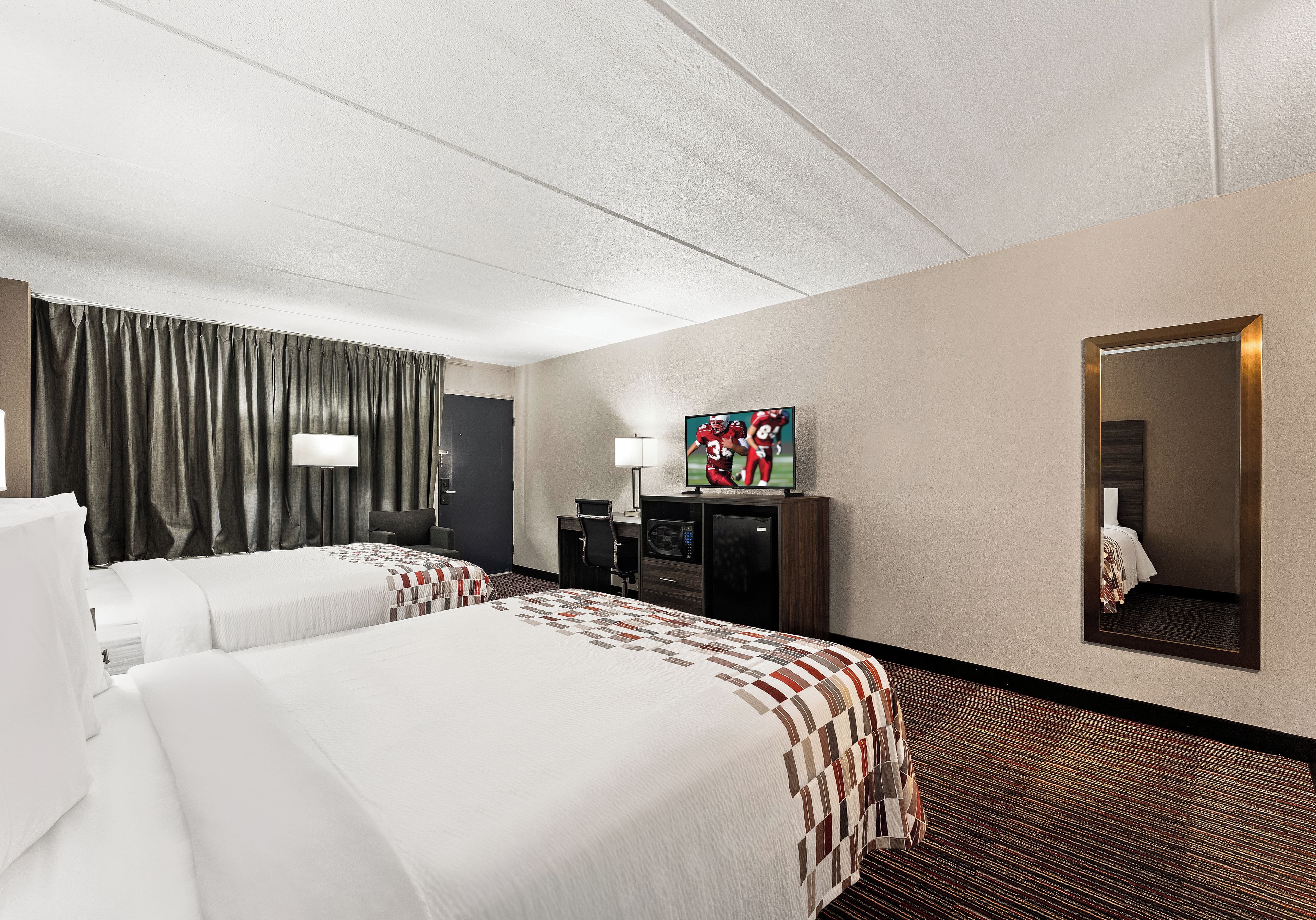 Habitación de hotel con dos camas, un escritorio, televisión y espejo.