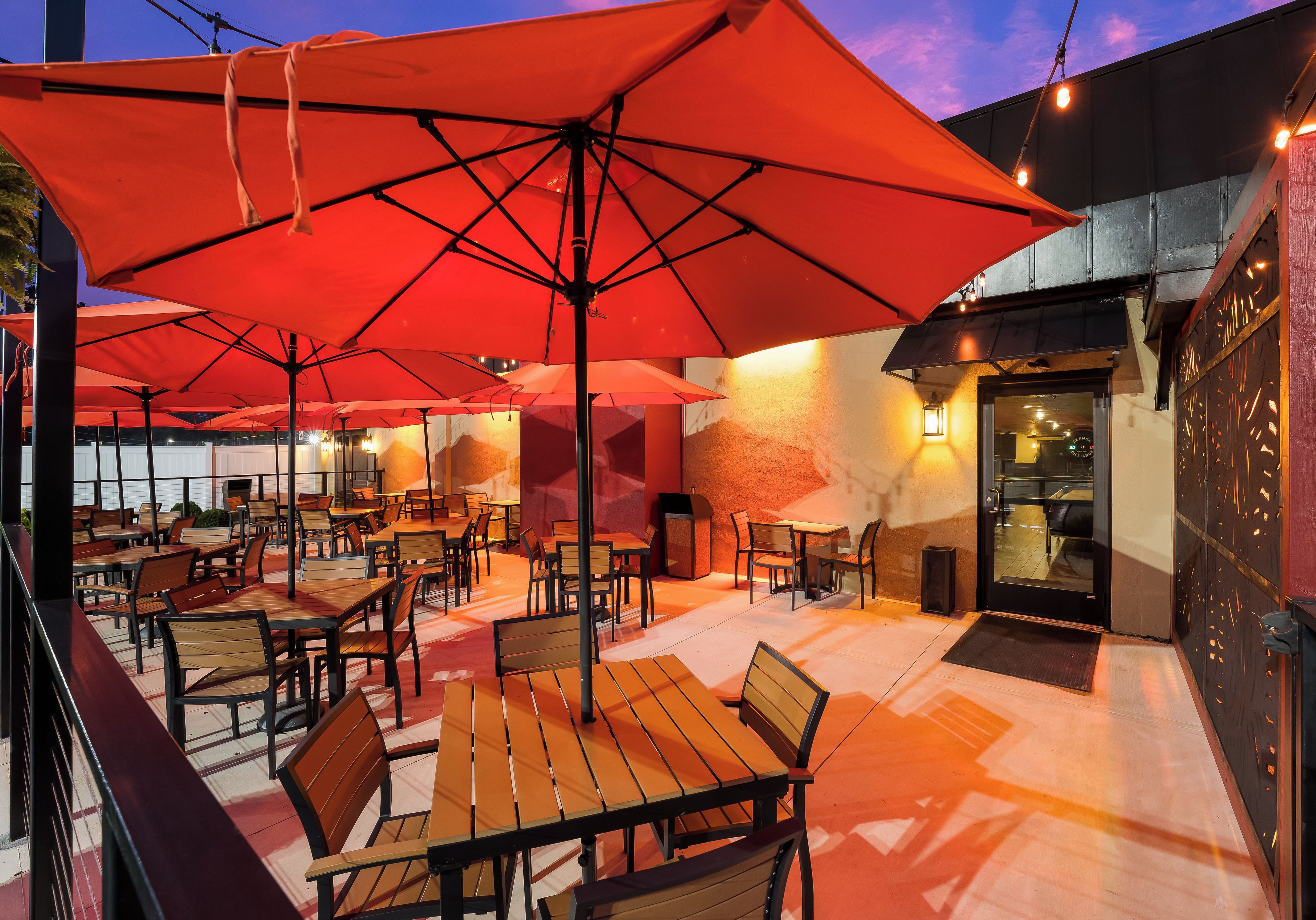 An outdoor seating area with multiple tables and chairs, covered by large red umbrellas.