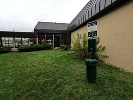 Fachada de edificio con un letrero que indica limpiar después de los perros, un bote de basura y un contenedor verde para reciclaje.