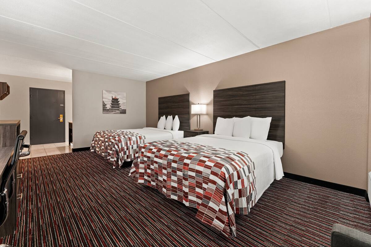 Una habitación de hotel con dos camas, un escritorio, una silla y una puerta.