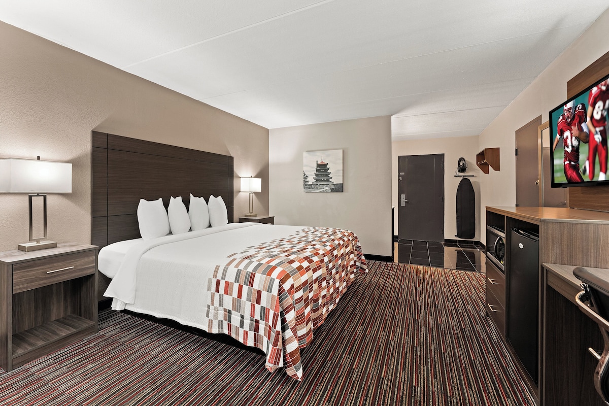 A hotel room with a large bed, a desk with a lamp, a television, and a cabinet.