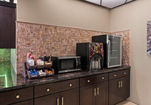 A kitchen area with a stone backsplash, a refrigerator, a microwave, and a coffee maker.