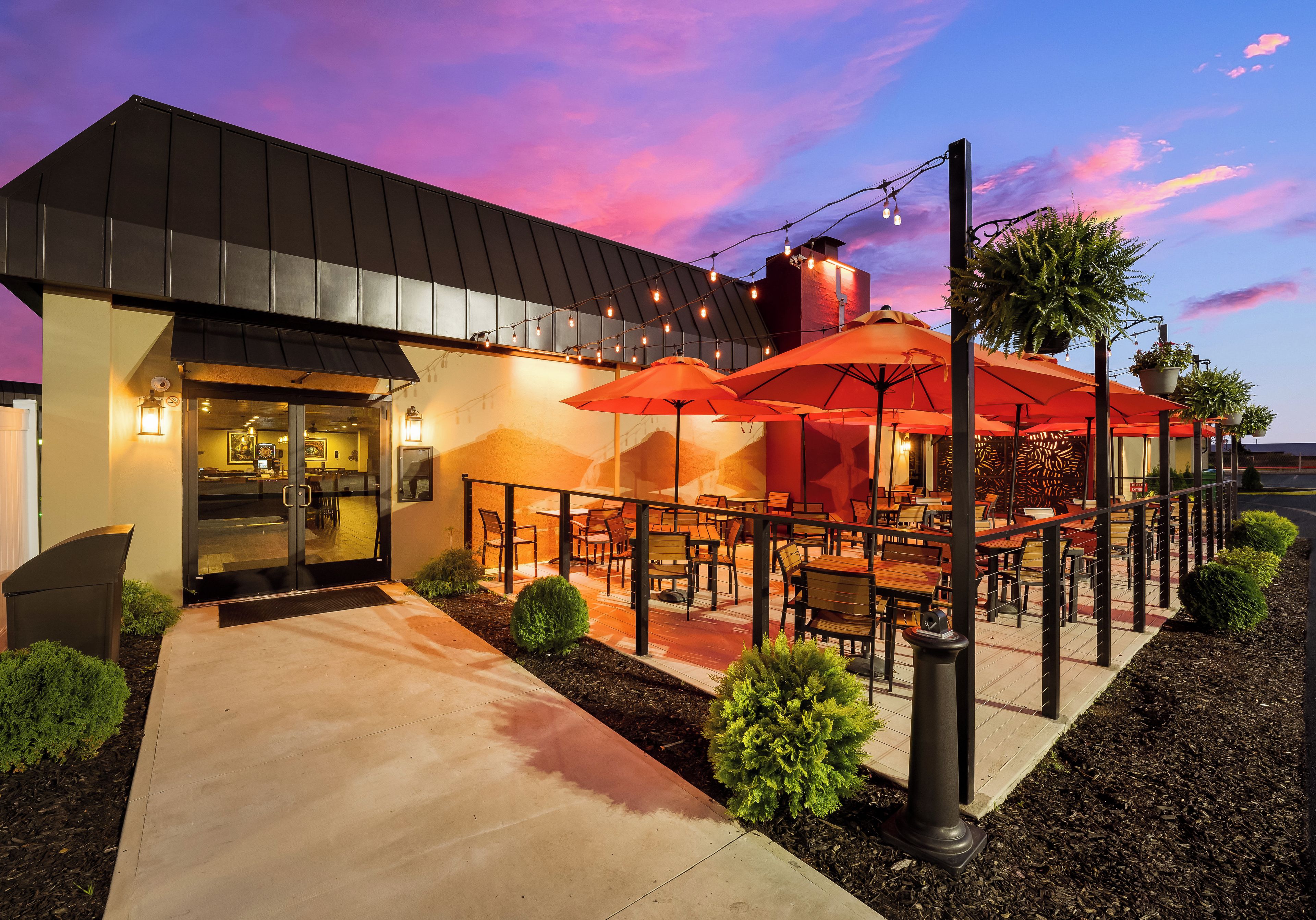 An outdoor seating area with tables and chairs, a covered patio, and a building with a glass entrance.