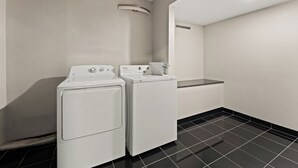 A laundry room with two white front-loading washers and dryers, a black tiled floor, and a white ceiling with a recessed light fixture. - Red Roof Inn Reading (Reading)
