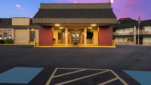 A building with a flat roof, a front entrance with a bench, and a parking lot with marked spaces. - Red Roof Inn Reading (Reading)