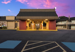 A building with a flat roof, a front entrance with a bench, and a parking lot with marked spaces. - Red Roof Inn Reading (Reading)