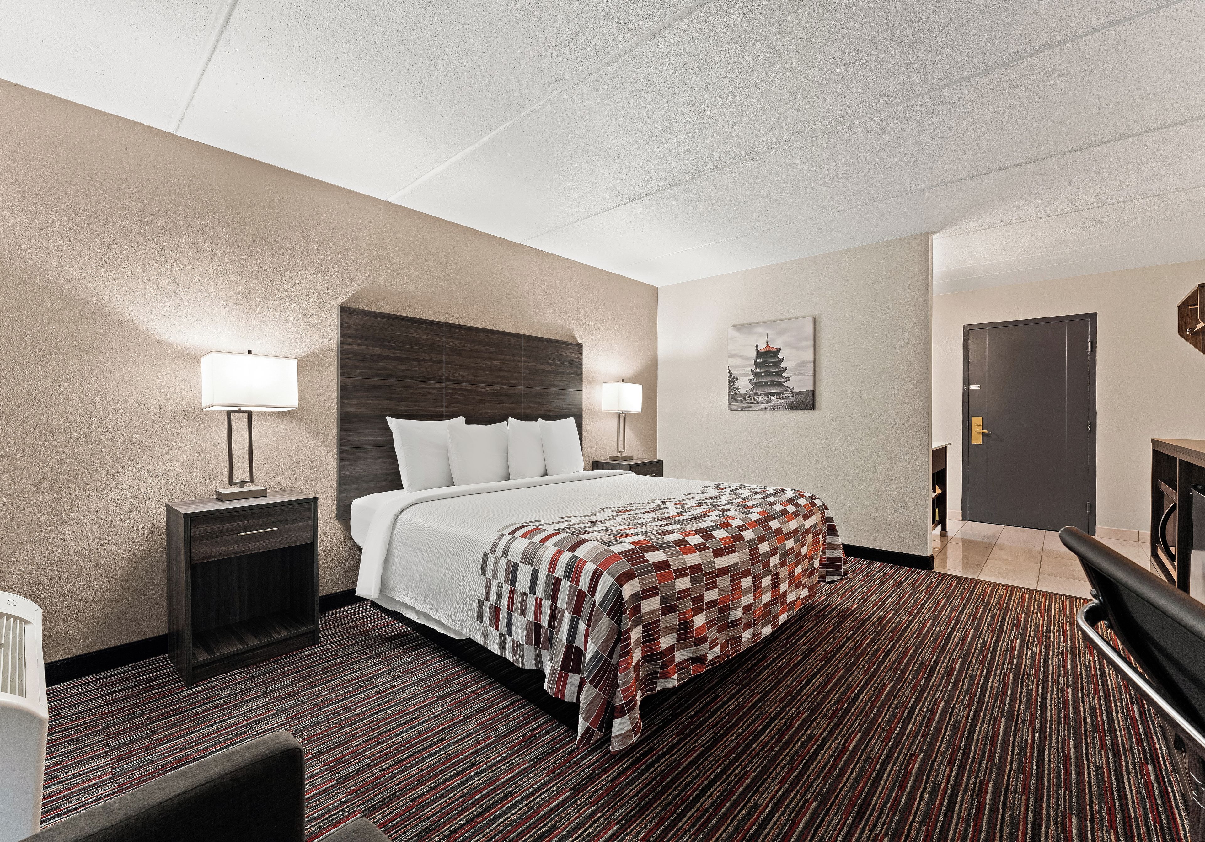 A hotel room with a bed, bedside tables, a lamp, a painting, and a door.