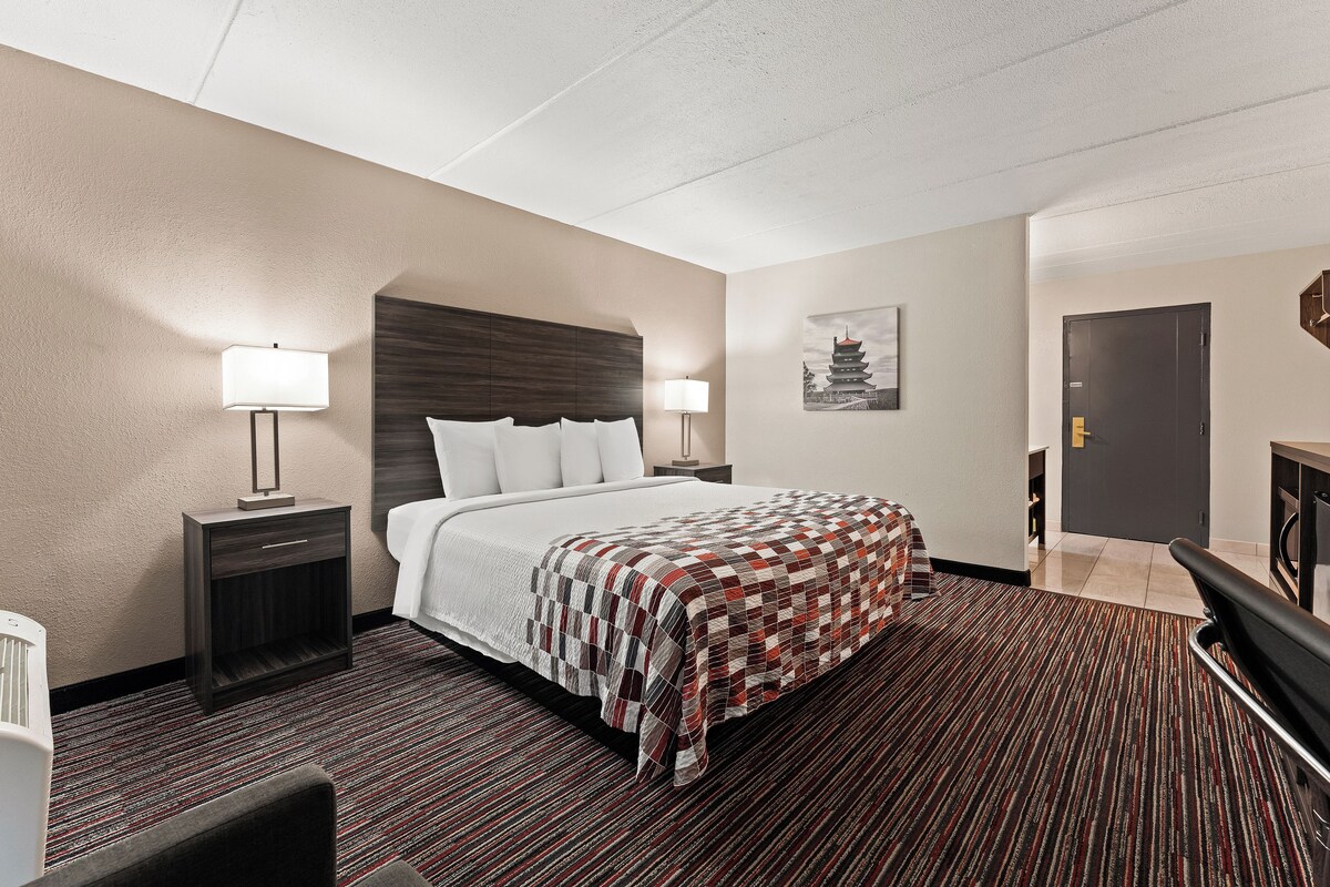 A hotel room with a bed, bedside tables, a lamp, a painting, and a door.