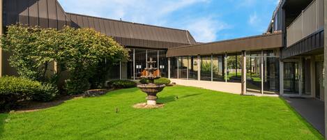 A courtyard with a fountain, a building with large windows, and a well-maintained lawn.