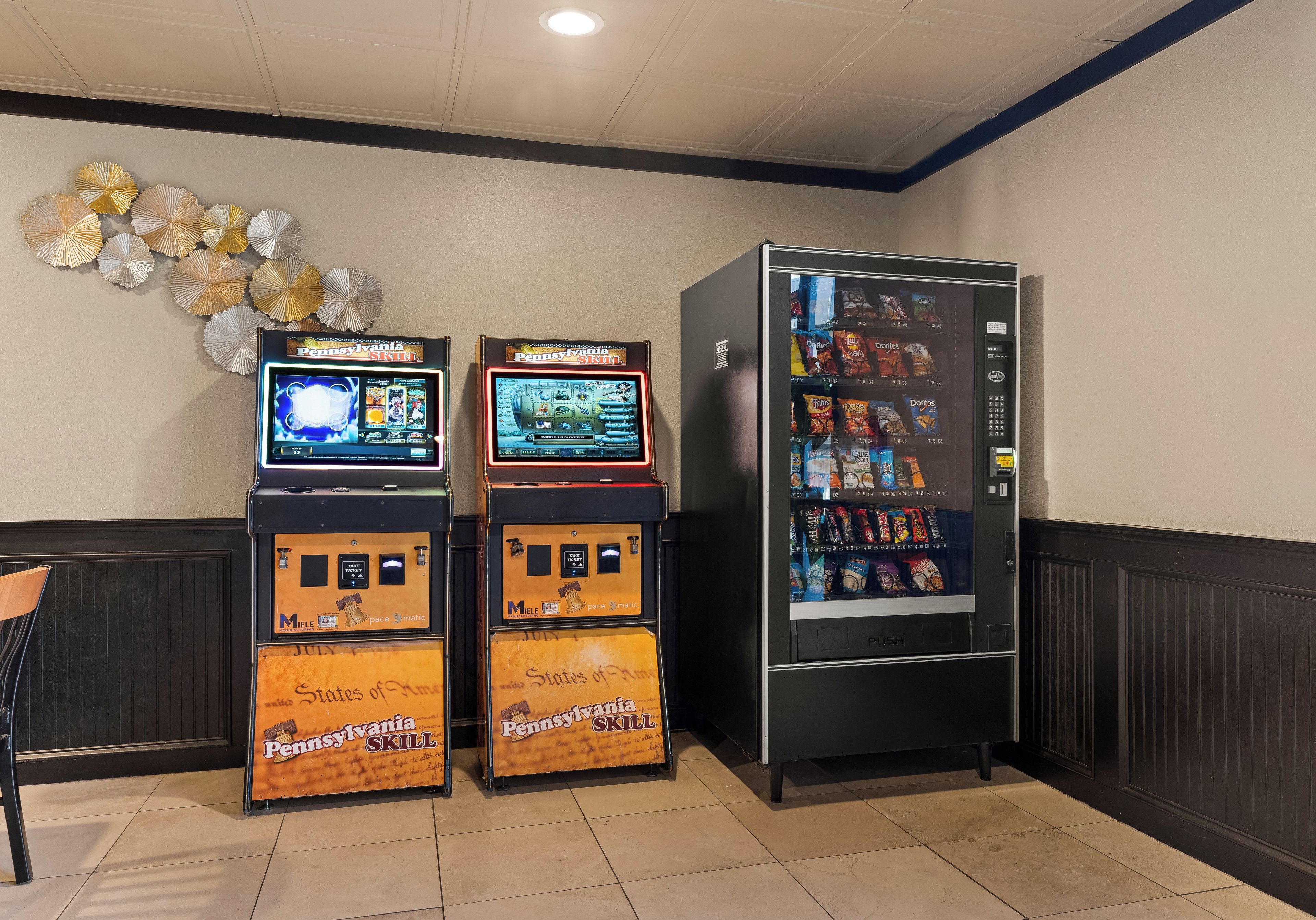 A vending machine and two slot machines in a room with tiled flooring and a decorative wall.