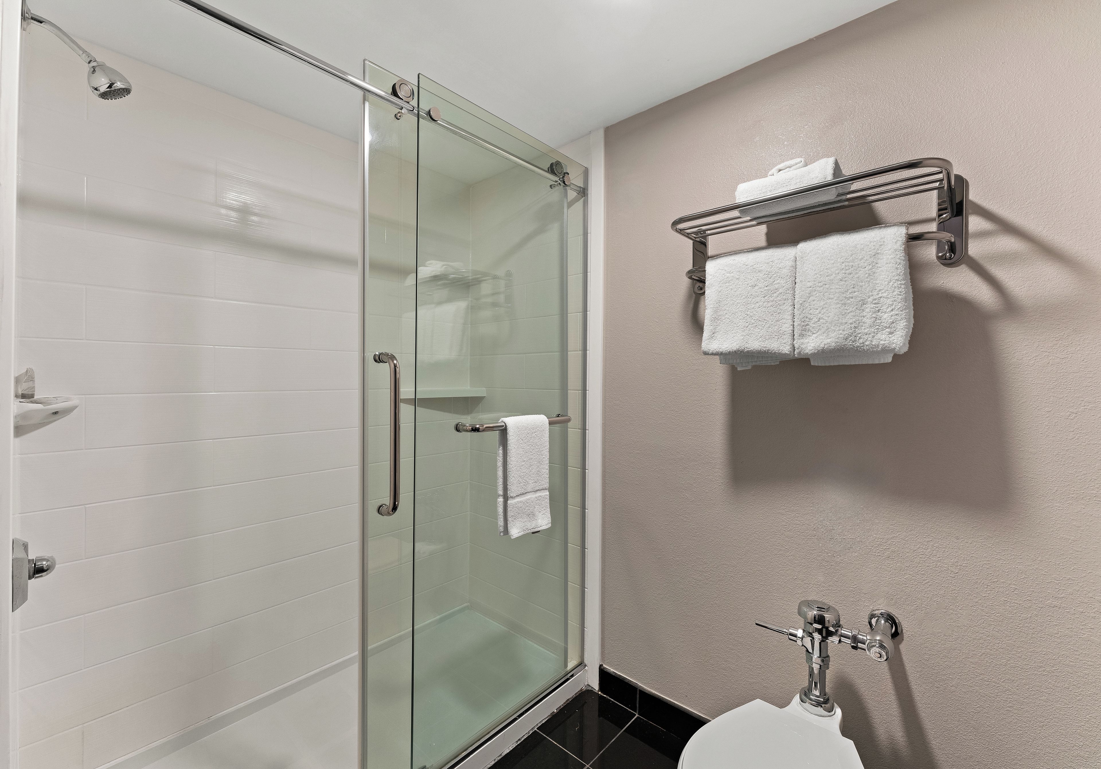 Un baño moderno con cabina de ducha de vidrio, un inodoro y un perchero con dos toallas.