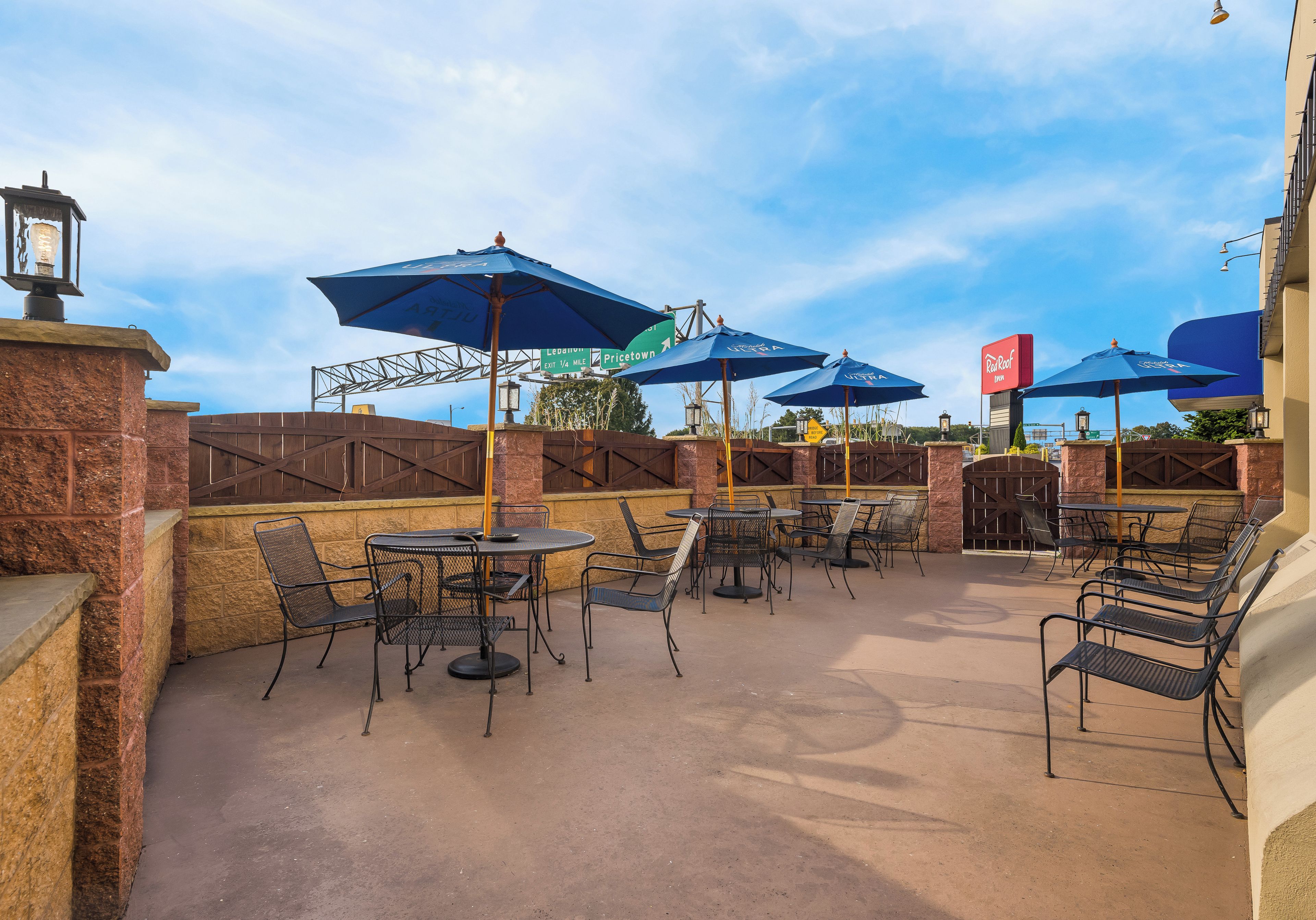 An outdoor patio area with tables and chairs, umbrellas, and a brick wall.