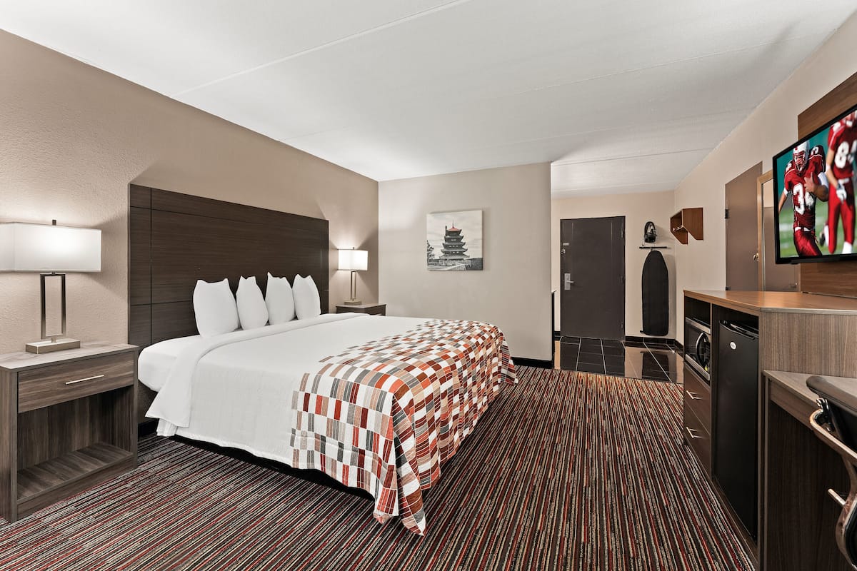 Una habitación de hotel con una cama grande, un escritorio con lámpara, un televisor y un armario.