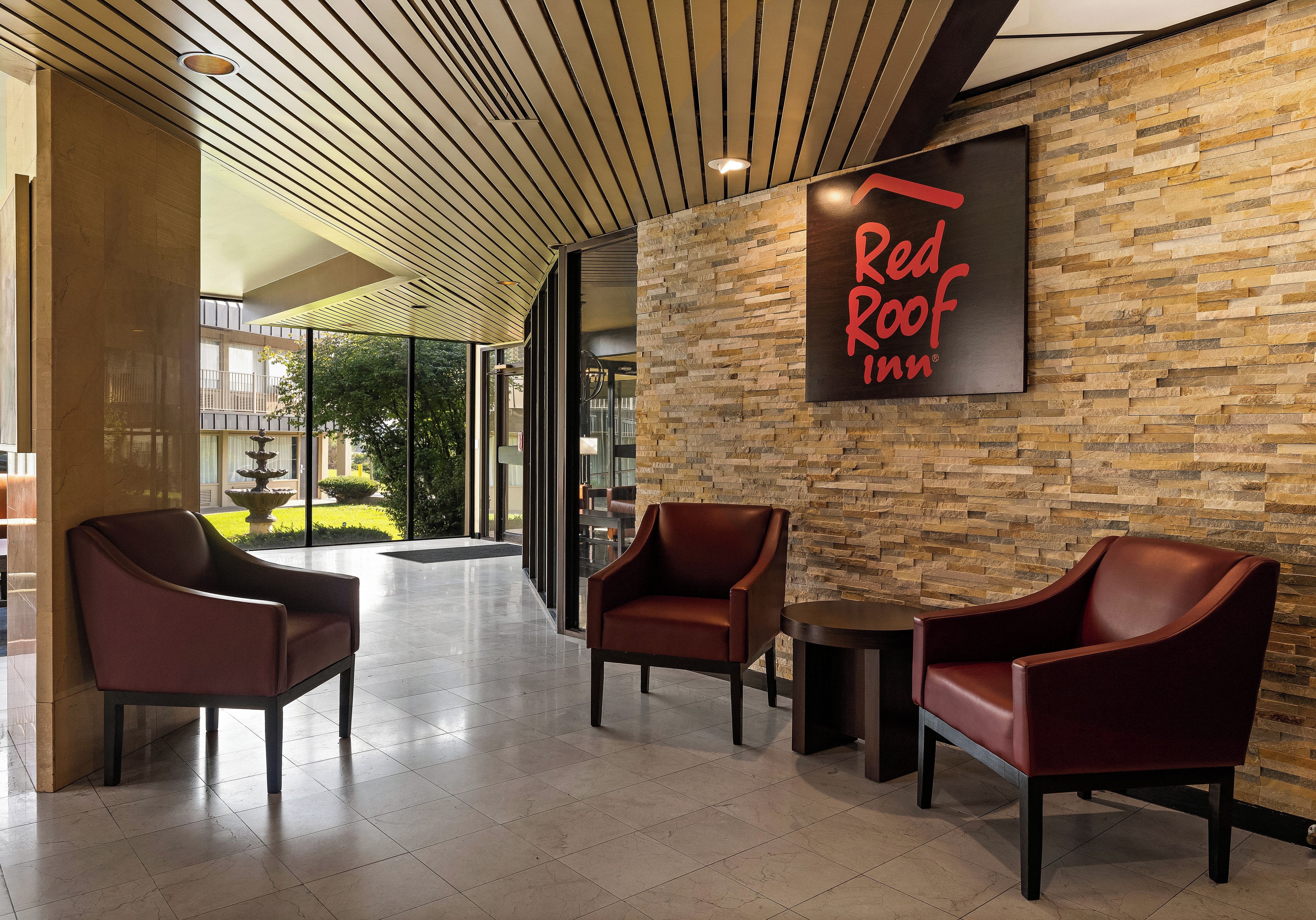 En lobby i ett Red Roof Inn-hotell med en vägg av sten, läderstolar och ett klinkergolv.