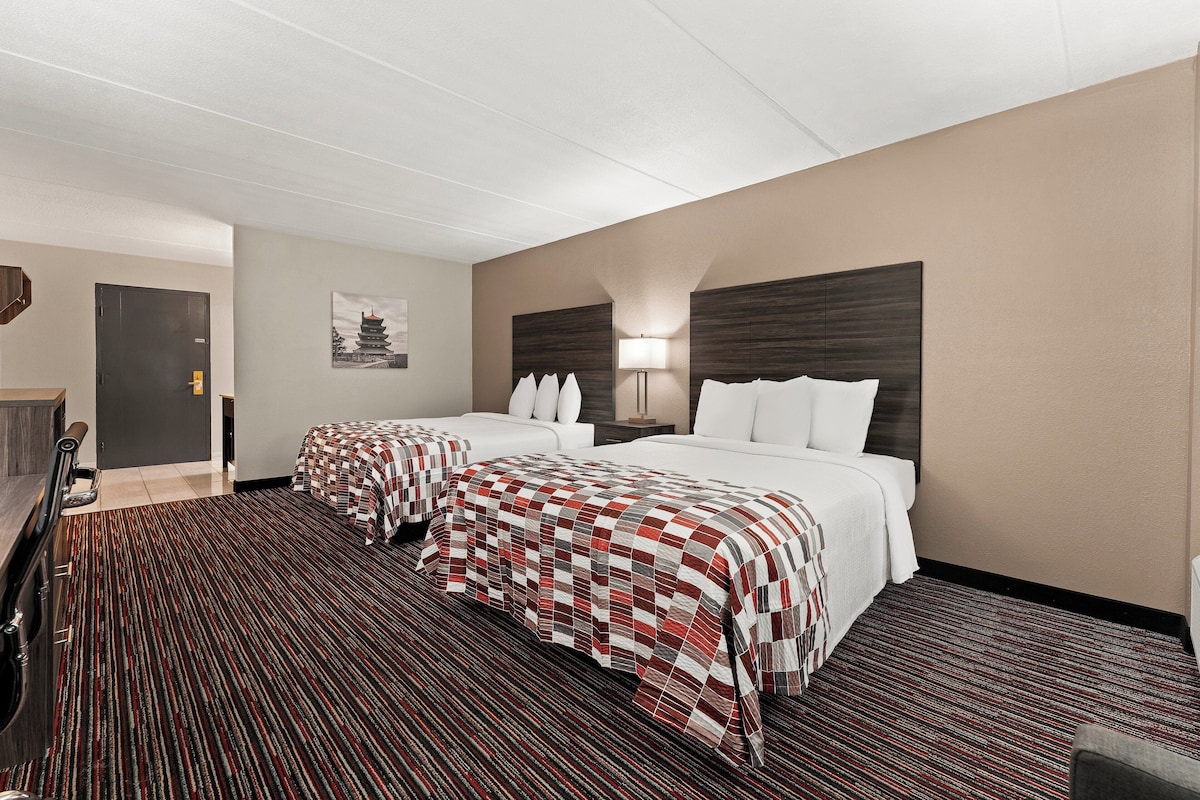 A hotel room with two beds, a desk, a chair, and a door.