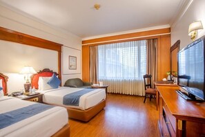 Habitació d'hotel amb dos llits, una taula de treball, televisió i una finestra gran amb cortines.