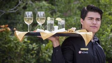A person carrying a tray with glasses of white wine, a lemon, and a dish of food.