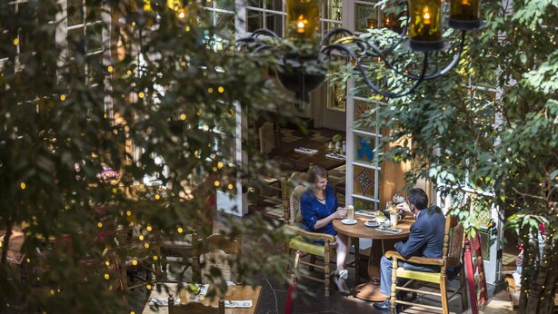 An indoor dining area with tables and chairs, surrounded by greenery and decorative lighting. - La Fonda on the Plaza (Santa Fe)
