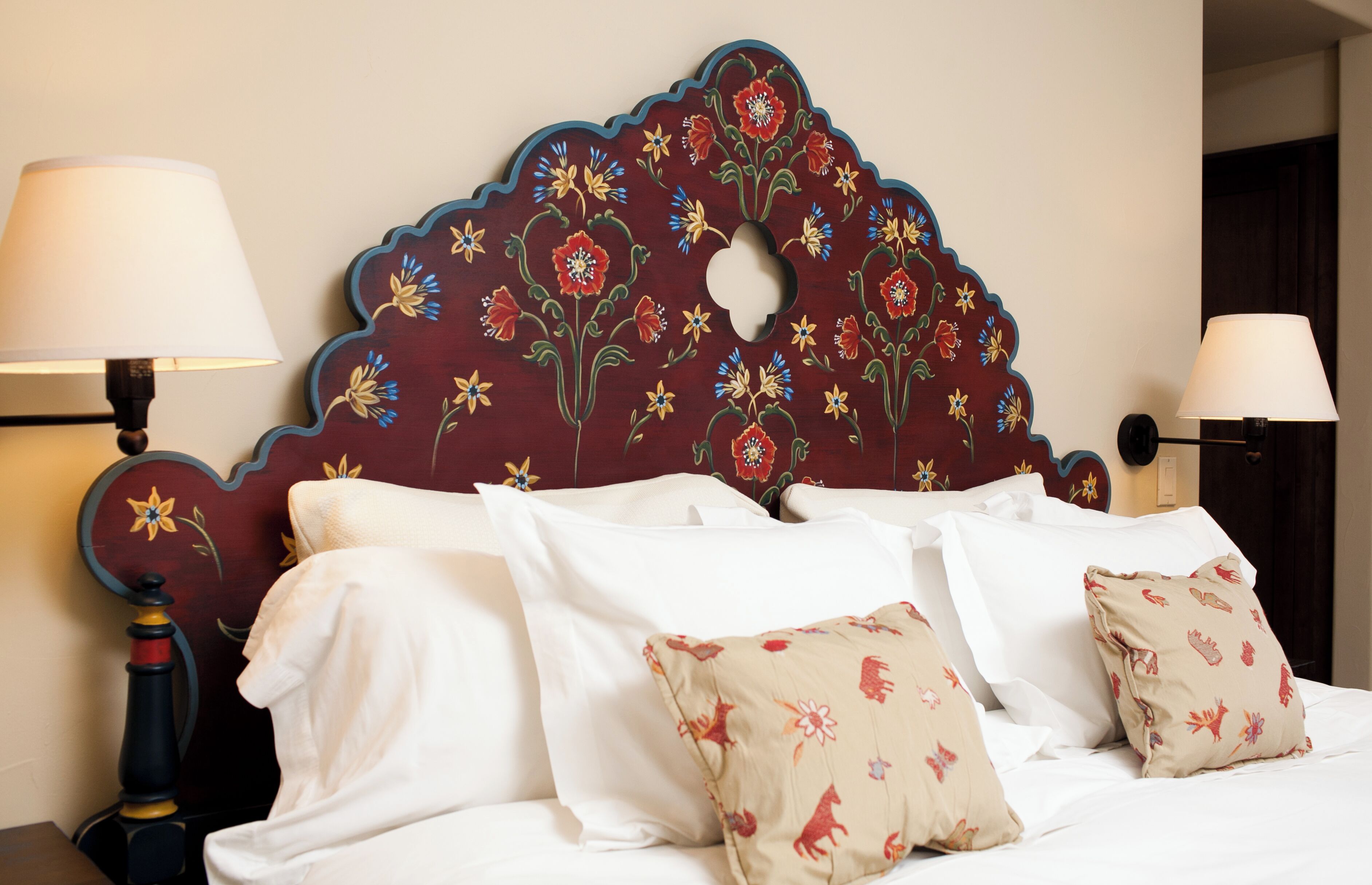 A bed with white linens and floral-patterned pillows, a wooden headboard with floral carvings, and two bedside lamps.