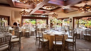 A spacious dining area with round tables and chairs, large hanging chandeliers, and a view through the windows. - La Fonda on the Plaza (Santa Fe)