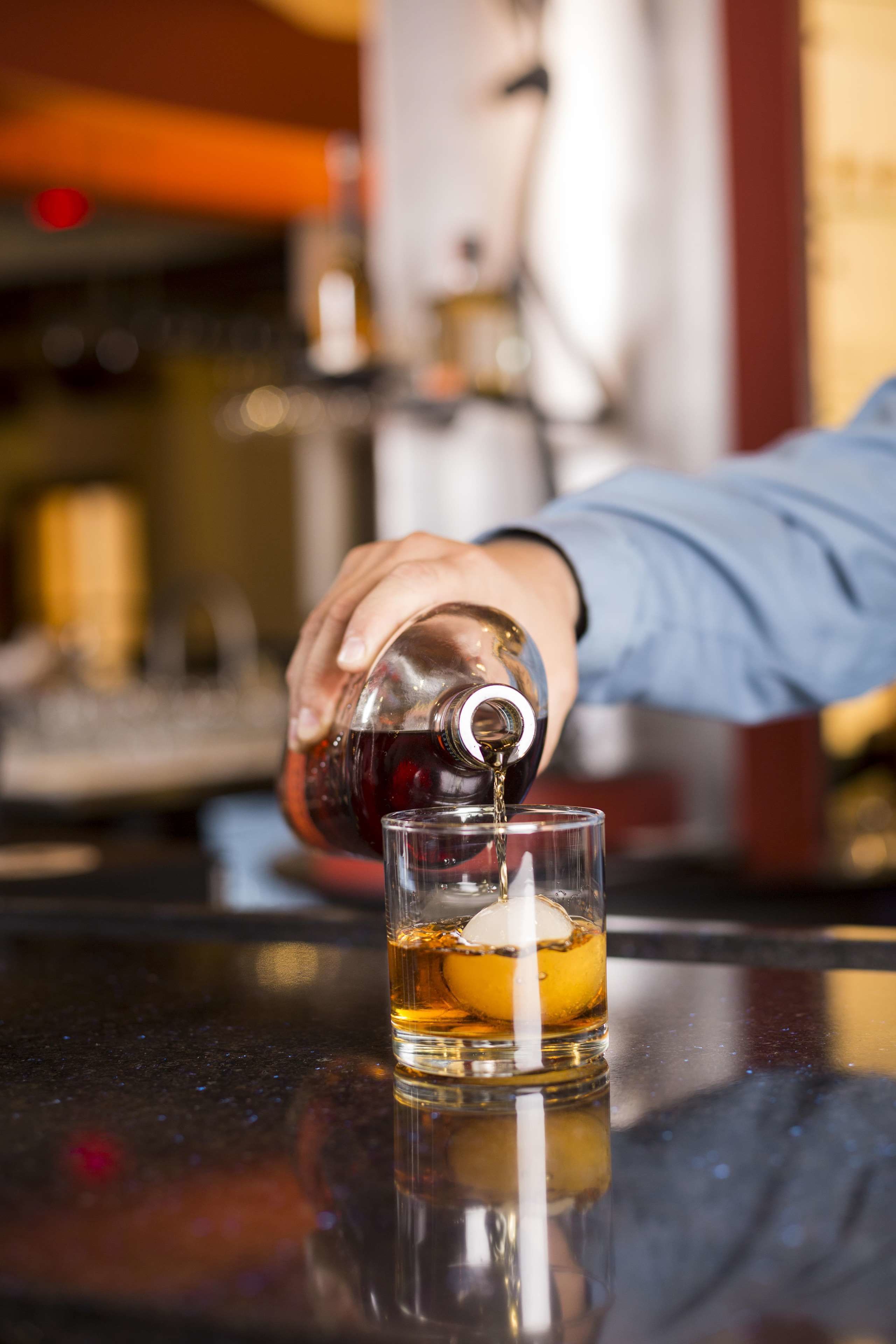 A hand pouring a drink into a glass with an orange slice.