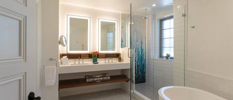 A modern bathroom with a glass-enclosed shower, a white bathtub, and a vanity with two mirrors.