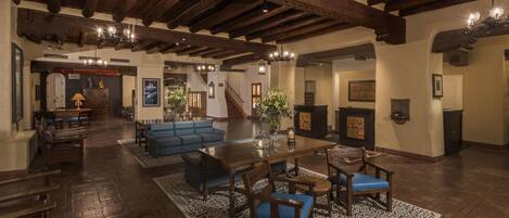 A spacious living area with a wooden ceiling, a large sofa, a dining table, and a patterned rug.