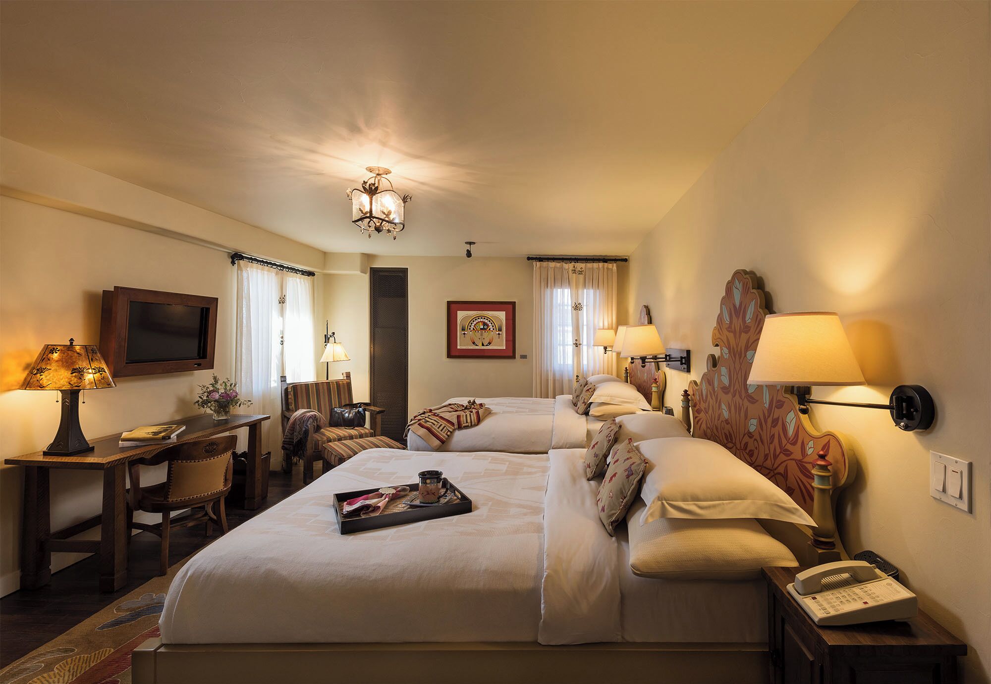A hotel room with two beds, a desk, a chair, a TV, lamps, and a telephone.
