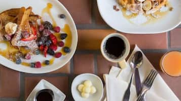 Une table dressée pour le petit-déjeuner, avec des gaufres, des crêpes et des fruits rouges disposés sur des assiettes, accompagnés de tasses de café et d’un pot de sirop.