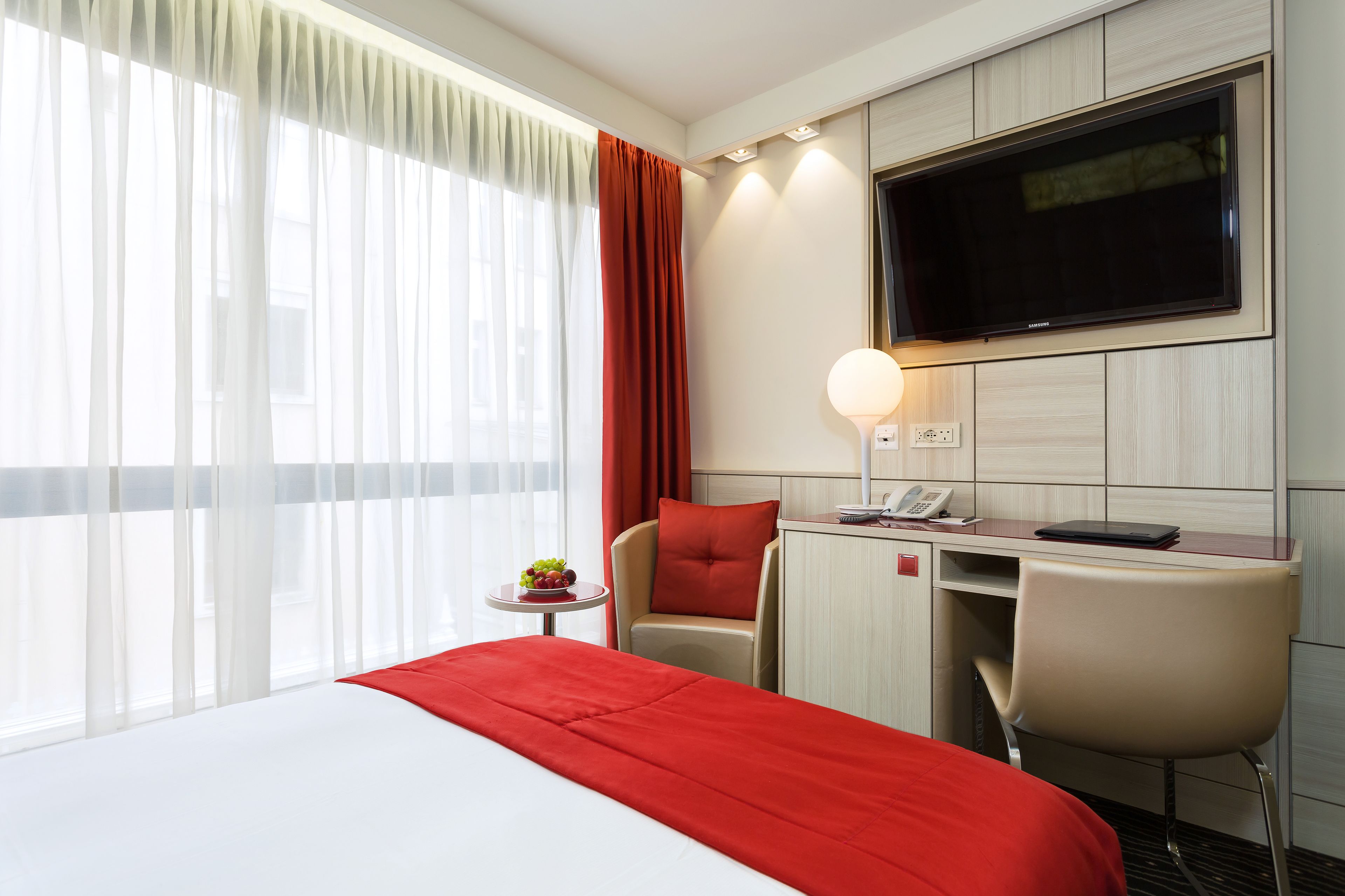 Une chambre d’hôtel avec un lit, un bureau et une chaise, une télévision et une petite table avec des fruits.