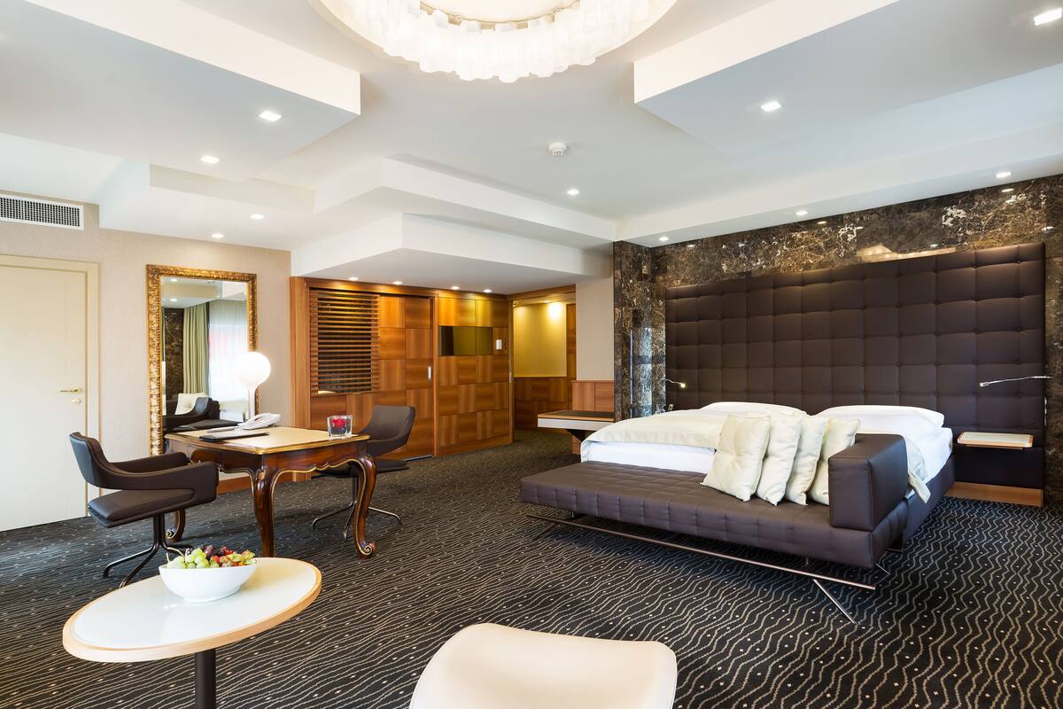 Habitación de hotel moderna con una cama grande, un escritorio, una silla y una pequeña mesa con un cuenco de fruta.