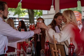 Un grupo de personas brindando con bebidas en un evento al aire libre, con varias botellas y copas sobre la mesa.