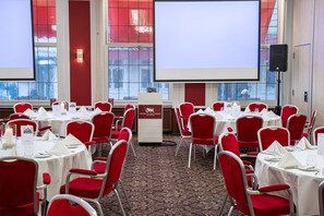 A conference room with red chairs, white tables, and a large screen at the front. - St Gotthard Hotel (Zürich)