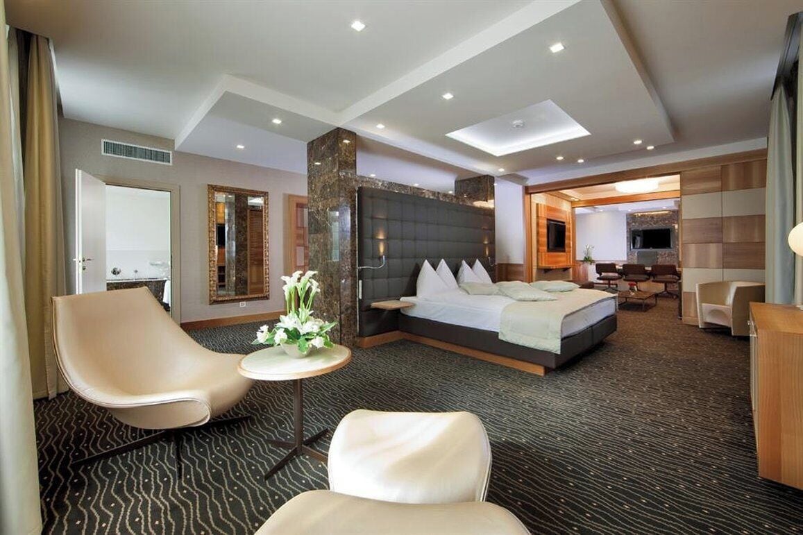 Ein Hotelzimmer mit einem großen Bett, einer Sitzecke mit Stühlen, einem kleinen Tisch mit Blumen und einem Fernseher.
