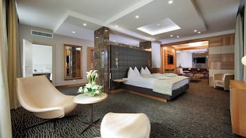 Ein Hotelzimmer mit einem großen Bett, einer Sitzecke mit Stühlen, einem kleinen Tisch mit Blumen und einem Fernseher.