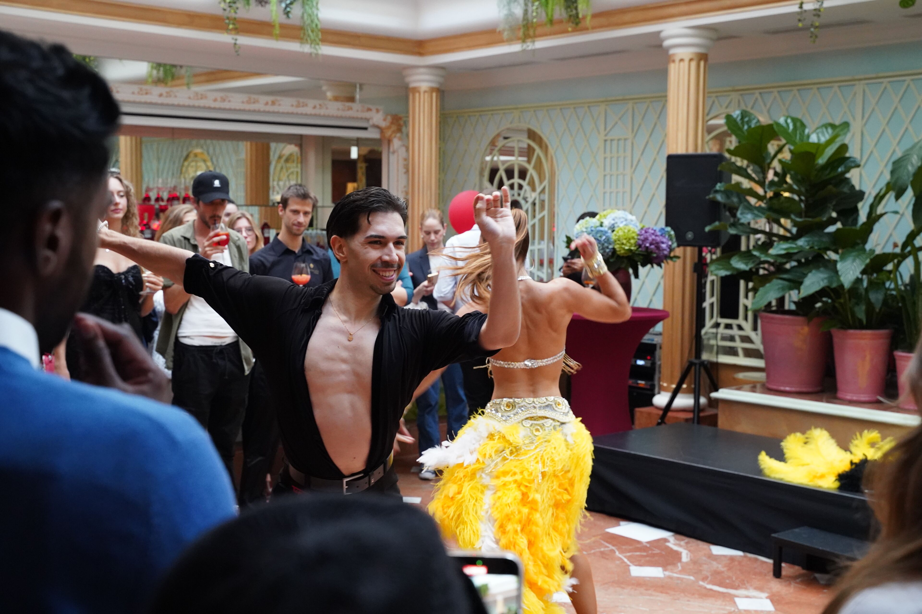 Un salón de baile con escenario, columnas y plantas en macetas.
