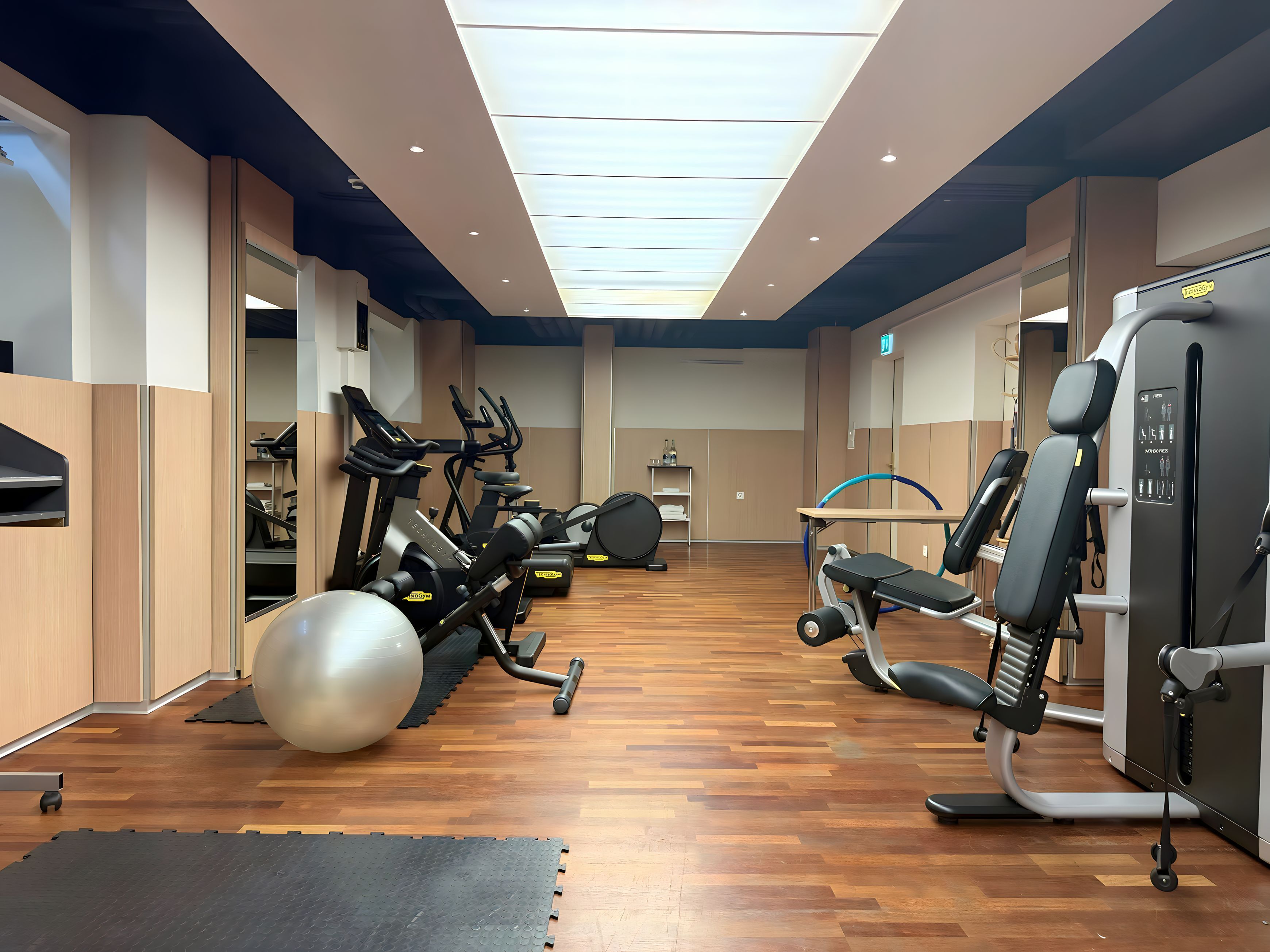 A gym with exercise equipment, wooden flooring, and a skylight ceiling.