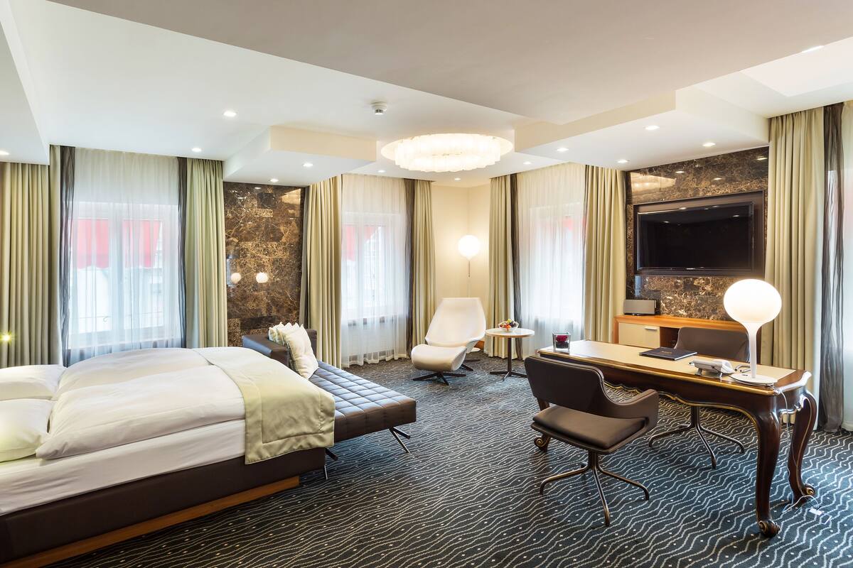 Habitación de hotel con una cama grande, un escritorio, una silla, un televisor y una pequeña mesa con lámpara.