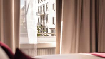 A hotel room with a bed, curtains, and a view of a building with multiple windows.