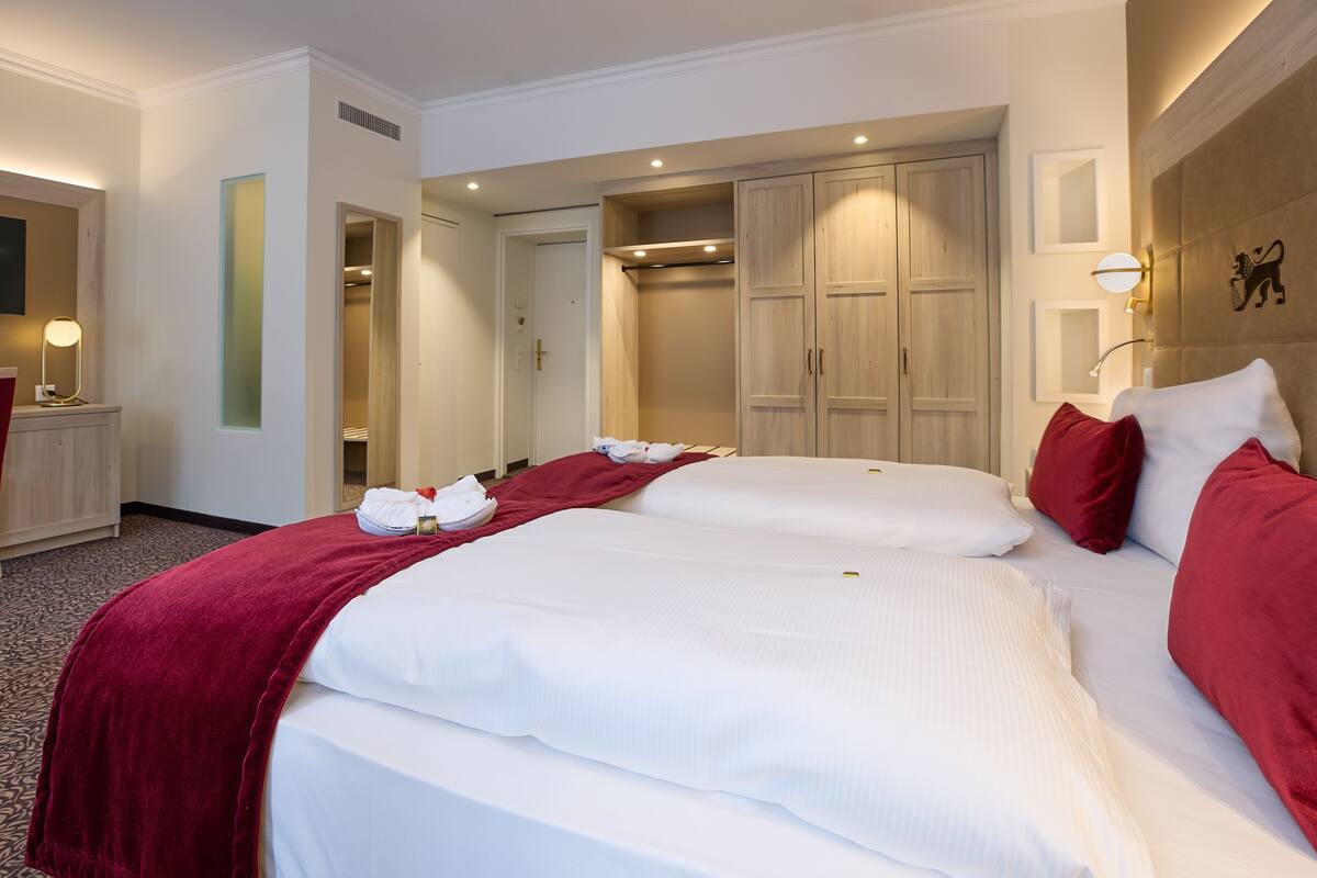 Una habitación de hotel con dos camas, un armario, un espejo y un pequeño escritorio con lámpara.