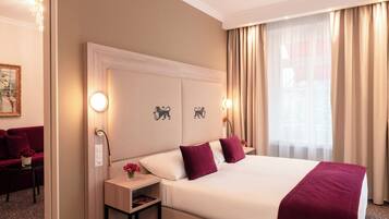 Habitación de hotel con una cama grande, dos mesitas de noche, una lámpara de pared, un cuadro y una ventana con cortinas.