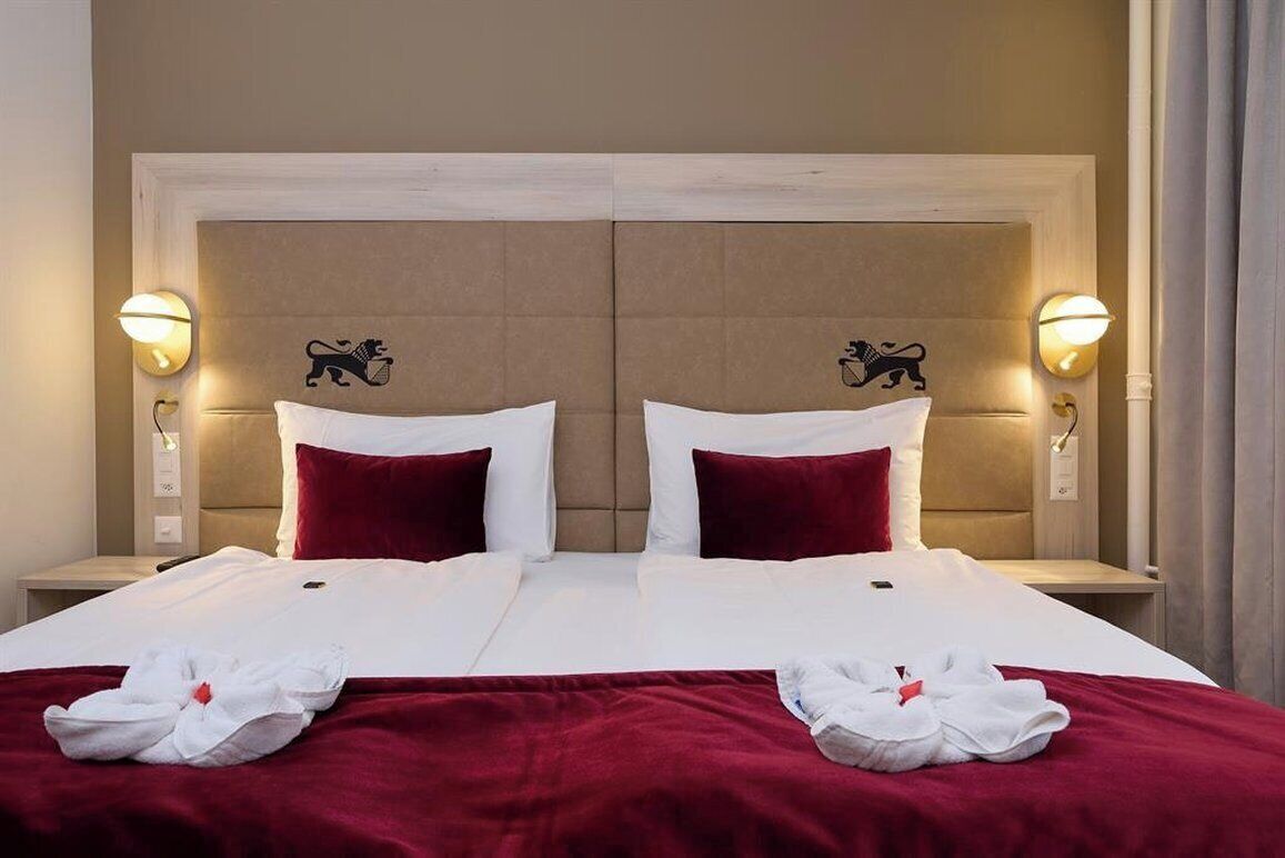 Ein Hotelzimmer mit einem Doppelbett, zwei Kissen, einer roten Decke und zwei Wandlampen mit Löwenmotiven.