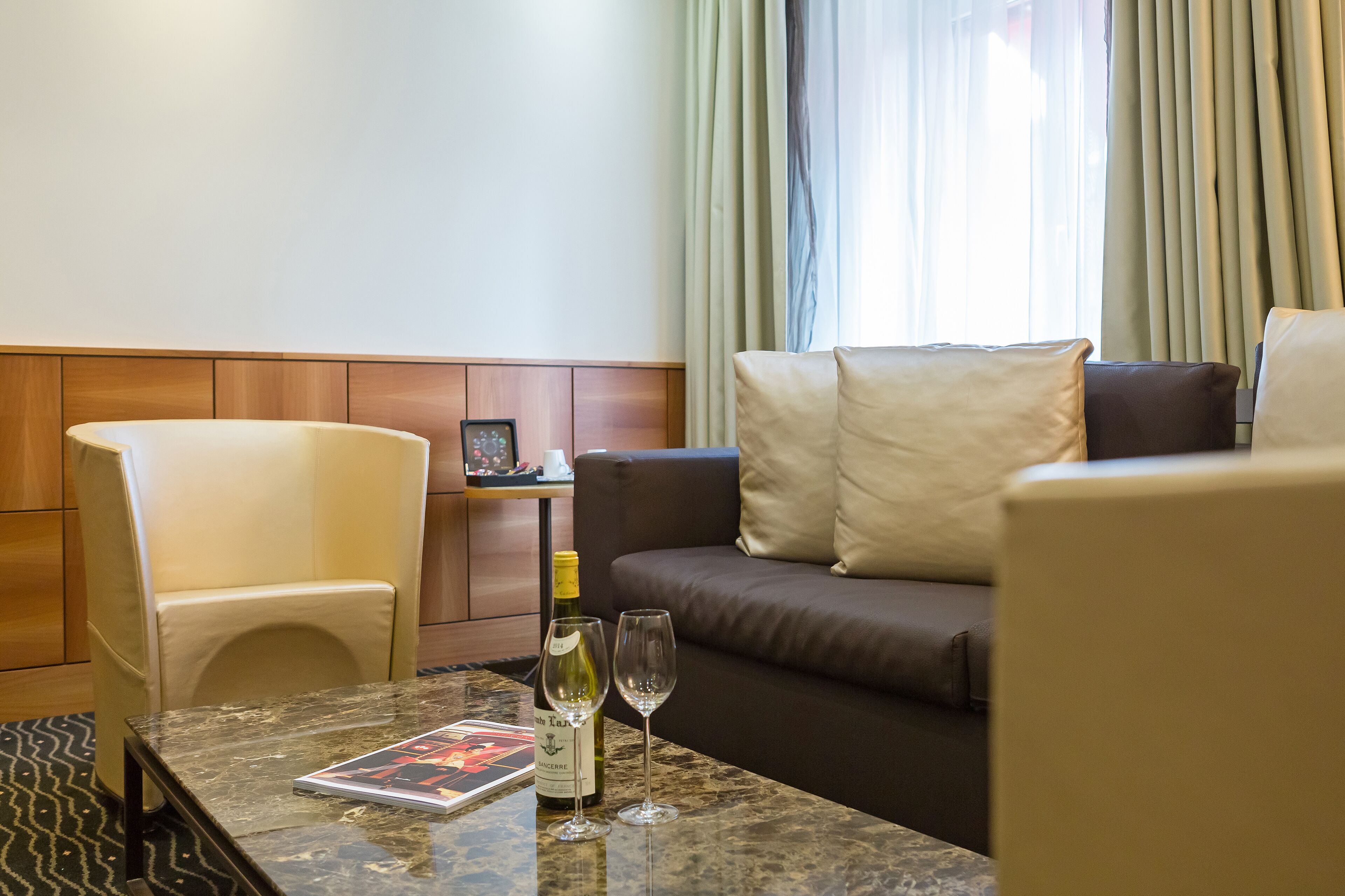 A hotel room with a marble table, a sofa, a chair, and a window with curtains.
