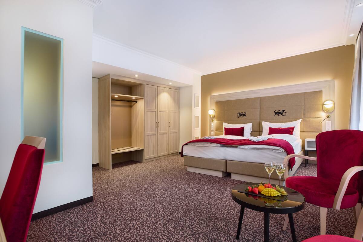 Una habitación de hotel con una cama, una silla roja, una mesita con fruta y un armario.