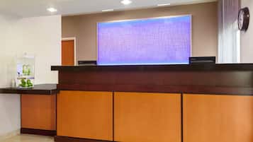Un mostrador de recepción con una pantalla digital, un acuario de cristal y un reloj en la pared.